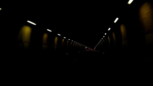blurred video 4K dark road through mountains, car drives through long, dark, lamp-lit tunnel in swiss alps, lights flicker, go into distance, auto travel concept, traffic, light at end of tunnel