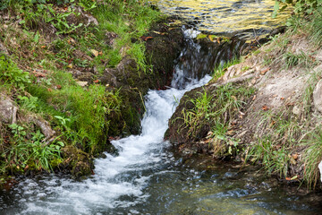 Streaming water, flowing through the rocks of a mountain alpine stream brook, with a speed blur on the water gurgling due to the movement of the flow. ..