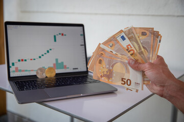 Hand of a Trader with some Euro banknotes and Bitcoin and Ethereum coins with green charts in the...