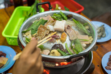 Assorted meat, mushrooms, and culantro (eryngium) being cooked on Thai fire pot (maw fai) at a self-service restaurant in Bangkok, Thailand.
