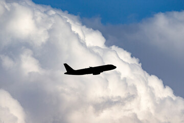 Commercial airliner aircraft flying at high altitude towards large white fluffy clouds.