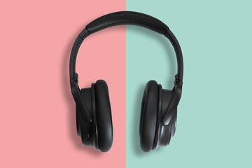 Computer headphones. Black headphones on a green-red pastel background. The concept of listening to music, creating audio, music. Computer work, abstraction and minimalist style.