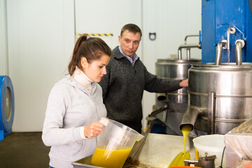 Confident couple controlling quality of traditional cold pressing olive oil on artisanal factory