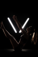 Fit woman practicing yoga poses. Silhouette girl doing exercise in studio against black background with v shaped white led tube light. No stress inner balance concept..