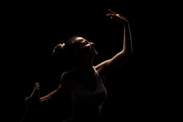 Fit girl practicing yoga in a studio. Half silhouette side lit fitness model.