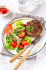 Beef hamburger with lettuce tomato salad on white plate, top view