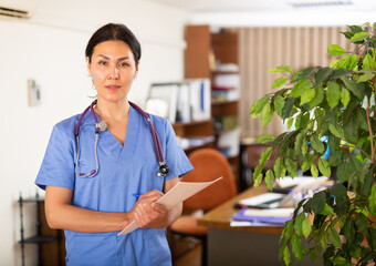 Portrait of confident woman doctor in blue overall working in clinic office