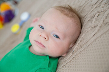 A blue-eyed baby in green clothes lies on a knitted homemade plaid