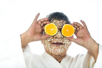 facial care Elderly latin woman applying an oatmeal mask and an orange slice to her face