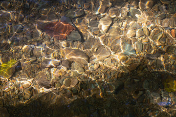 Background image of brown pebbles in a low flowing stream with soft morning sunlight. Gives a feeling of freshness in nature.