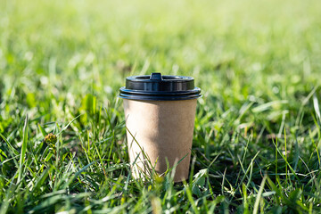 Mock up to go coffee cup against green grass. Template disposable craft cardboard takeaway coffee...