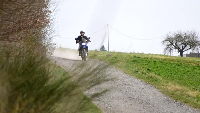 An off-road motorcycle rider stirring up dust while approaching on a dirt road in the countryside. Static frontal view