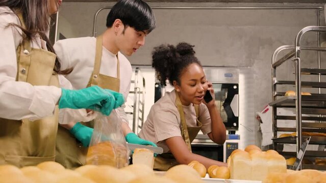 Three young friends and startup partners of bread dough and pastry foods busy with homemade baking jobs while cooking orders online, packing, and delivering on bakery shop, small business entrepreneur