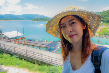 Happy young woman tourist in asian hat on lake and mountain vacation smiling at camera taking photo...