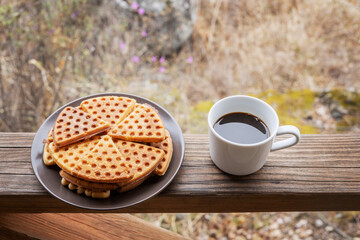 A plate of waffles and a mug of hot coffee stand on the wooden railing of the gazebo. 