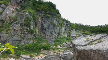 Steep hillsides against the sky. Green vegetation on the rocks. A large boulder in the foreground. Kamchatka
