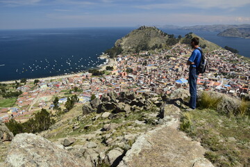A man on a hilltop looks at the landscape of Copacabana and Lake Titicaca. Copacabana, Bolivia