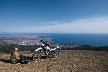 Female motorcyclist sitting and relaxing in offroad motorcycle travel on mountain top above ocean...