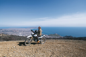 Female rider relaxing in enduro offroad motorcycle travel on mountain top, beautiful sea shore and...