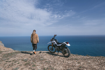 Woman relaxing with dirtbike on the top of mountain with stunning sea views