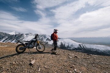 Fototapeta na wymiar Active man resting near dirt bike looking on beautiful snow mountain landscape
