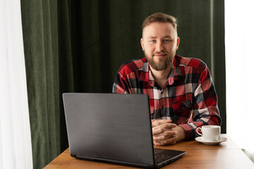 Portrait of happy male employee smiling at camera while working on laptop in home office or cafe