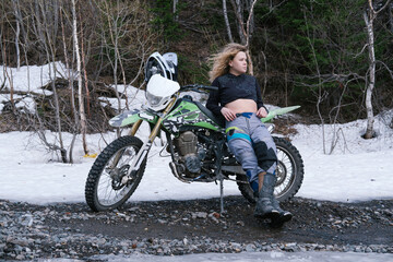 Beautiful woman motorcyclist standing near enduro motorcycle on resting while traveling through...