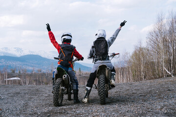 Happy Motorcyclists girls on dirt motorcycles wearing backpacks and moto protection equipment...