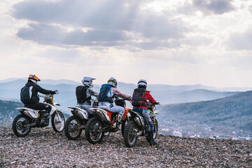 group of off-road dirt motorcyclists standing on edge of cliff  with a beautiful mountain valley ...