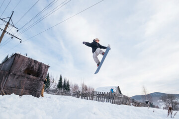 Naklejka na ściany i meble Snowboarder taking grab during jumping from abandoned building in wooden houses village