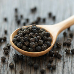 Whole black peppercorn in a wooden spoon on wooden background.