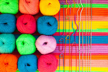 All for hand knitting. Knitted multi-colored handmade fabric with balls of multi-colored threads, pins and various knitting needles on it.