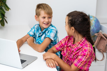 Young boy with a laptop computer sitting near a girl