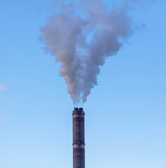 Smoke from chimneys at the plant in the rays of the sunset as a background.