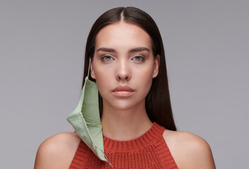 Portrait of serious attractive brunette woman with mask hanging on ear standing against gray...