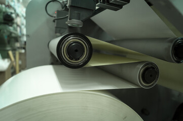 Paper alignment unit on the die-cutting machine for the production of self-adhesive labels in the printing house. Paper feeding on the rollers of the machine. Selective focus
