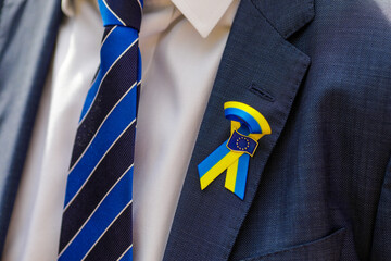 Shallow depth of field (selective focus) details with the Ukrainian flag and the European Union logo on the suit of a man.