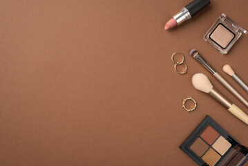 Makeup concept. Top view photo of eyeshadow palette gold rings lipstick and makeup brushes on isolated brown background with empty space