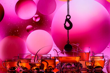 transparent glass teapot and cups with tea and drops on colorful background 