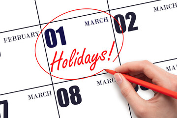 Hand drawing a red circle and writing the text Holidays on the calendar date 1 March. Important date.