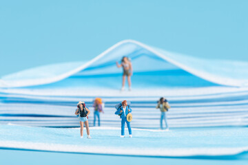 Miniature people travel with face mask on blue background,under Covid-19 pandemic,safety travels