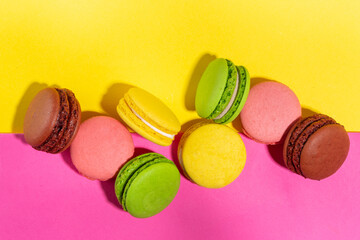 Brigth colorful (yellow, pink, green, brown) various flavor macarons sweet cookies on high-colored pink yellow background. Stack of small french macaron cakes, copy space flatlay