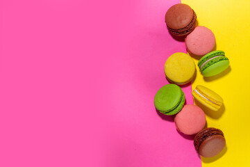 Brigth colorful (yellow, pink, green, brown) various flavor macarons sweet cookies on high-colored pink yellow background. Stack of small french macaron cakes, copy space flatlay