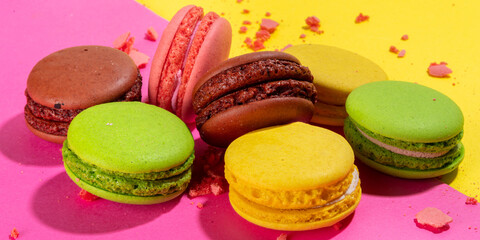 Fototapeta na wymiar Brigth colorful (yellow, pink, green, brown) various flavor macarons sweet cookies on high-colored pink yellow background. Stack of small french macaron cakes, copy space flatlay