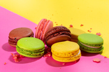 Fototapeta na wymiar Brigth colorful (yellow, pink, green, brown) various flavor macarons sweet cookies on high-colored pink yellow background. Stack of small french macaron cakes, copy space flatlay