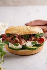 A bagel sandwich with pastrami, cucumber slices, watercress salad and ricotta on marble background