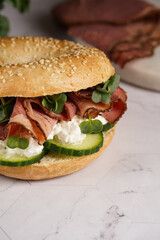A bagel sandwich with pastrami, cucumber slices, watercress salad and ricotta on marble background