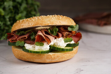 A bagel sandwich with pastrami, cucumber slices, watercress salad and ricotta on marble background