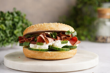 A bagel sandwich with pastrami, cucumber slices, watercress salad and ricotta on marble background
