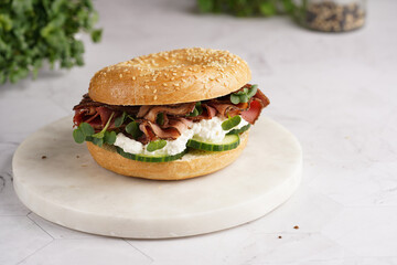 A bagel sandwich with pastrami, cucumber slices, watercress salad and ricotta on marble background